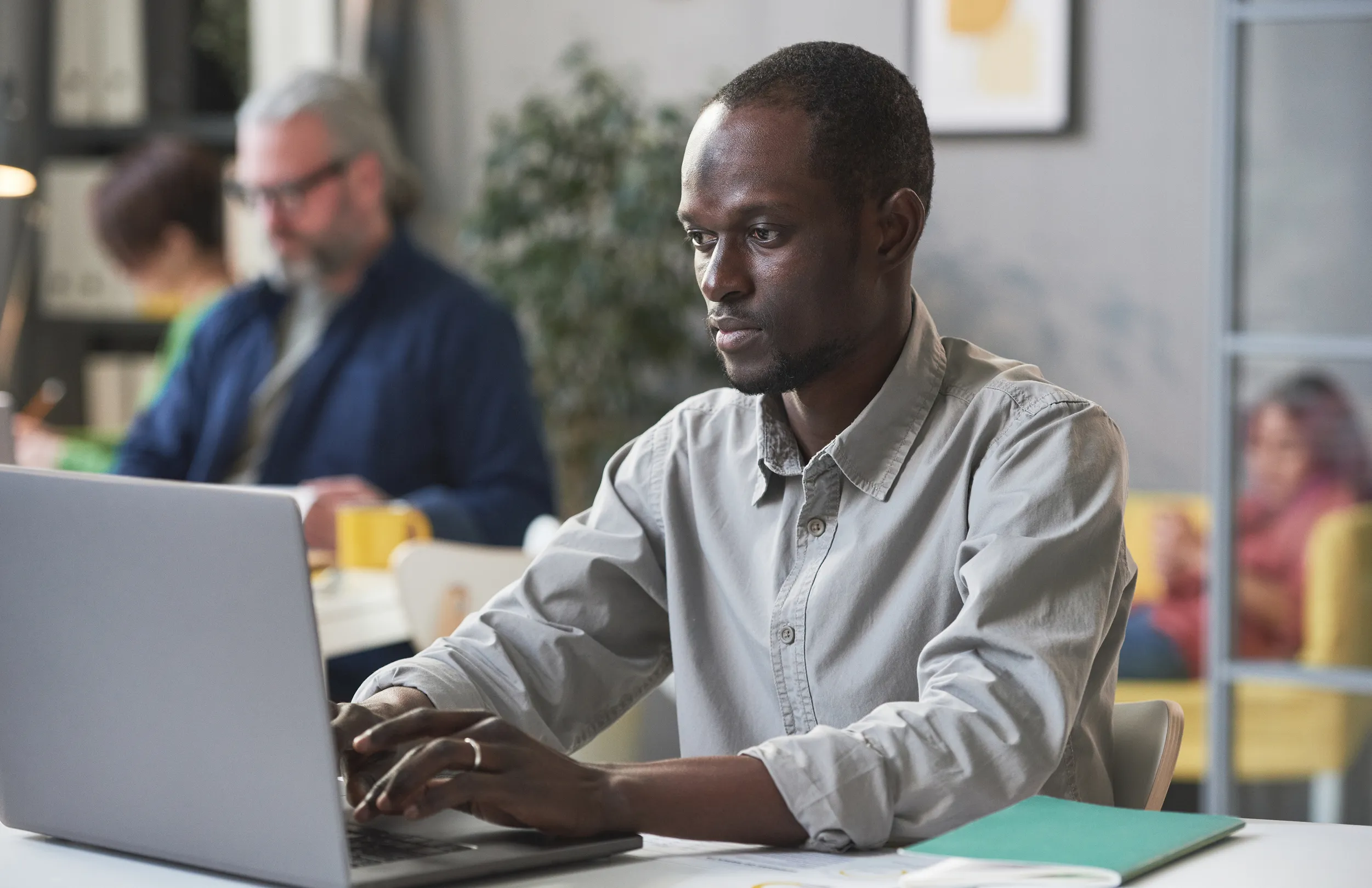 Man with short hair and beard working on a laptop at a desk in an office setting, focused on the screen.